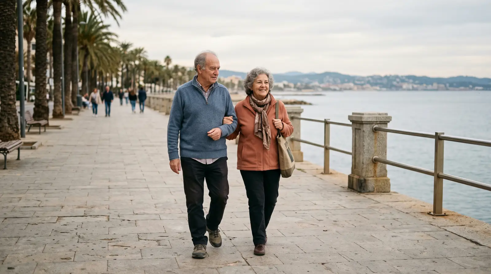 Una pareja de jubilados paseando del brazo por un paseo marítimo en otoño.
